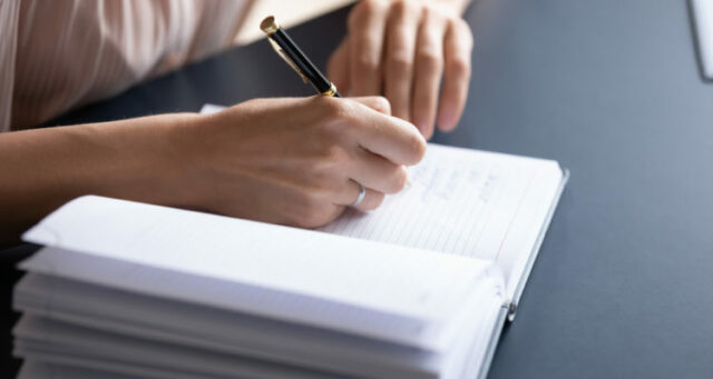 Close,Up,Young,Woman,Making,Notes,In,Notebook,,Sitting,At